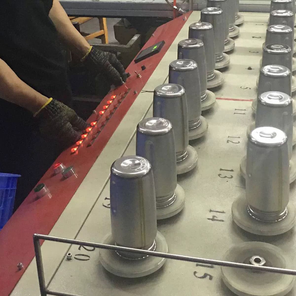 Inverted stainless steel tumbler bodies arranged at a production workstation