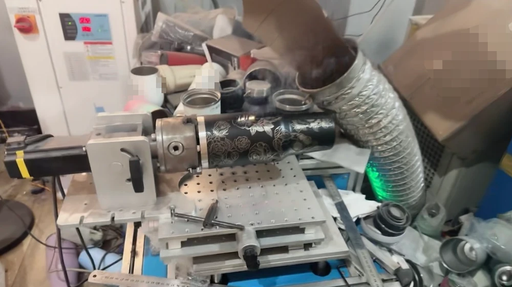 Dark patterned tumbler held in a rotary fixture beside an extraction hose