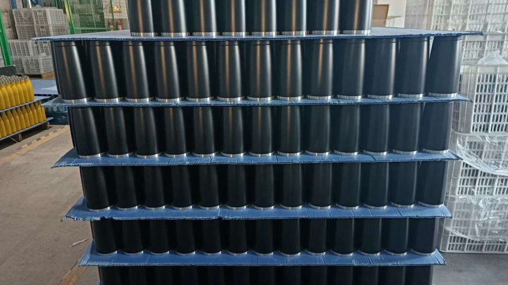 Rows of dark-coated drinkware bodies arranged on layered trays in the workshop