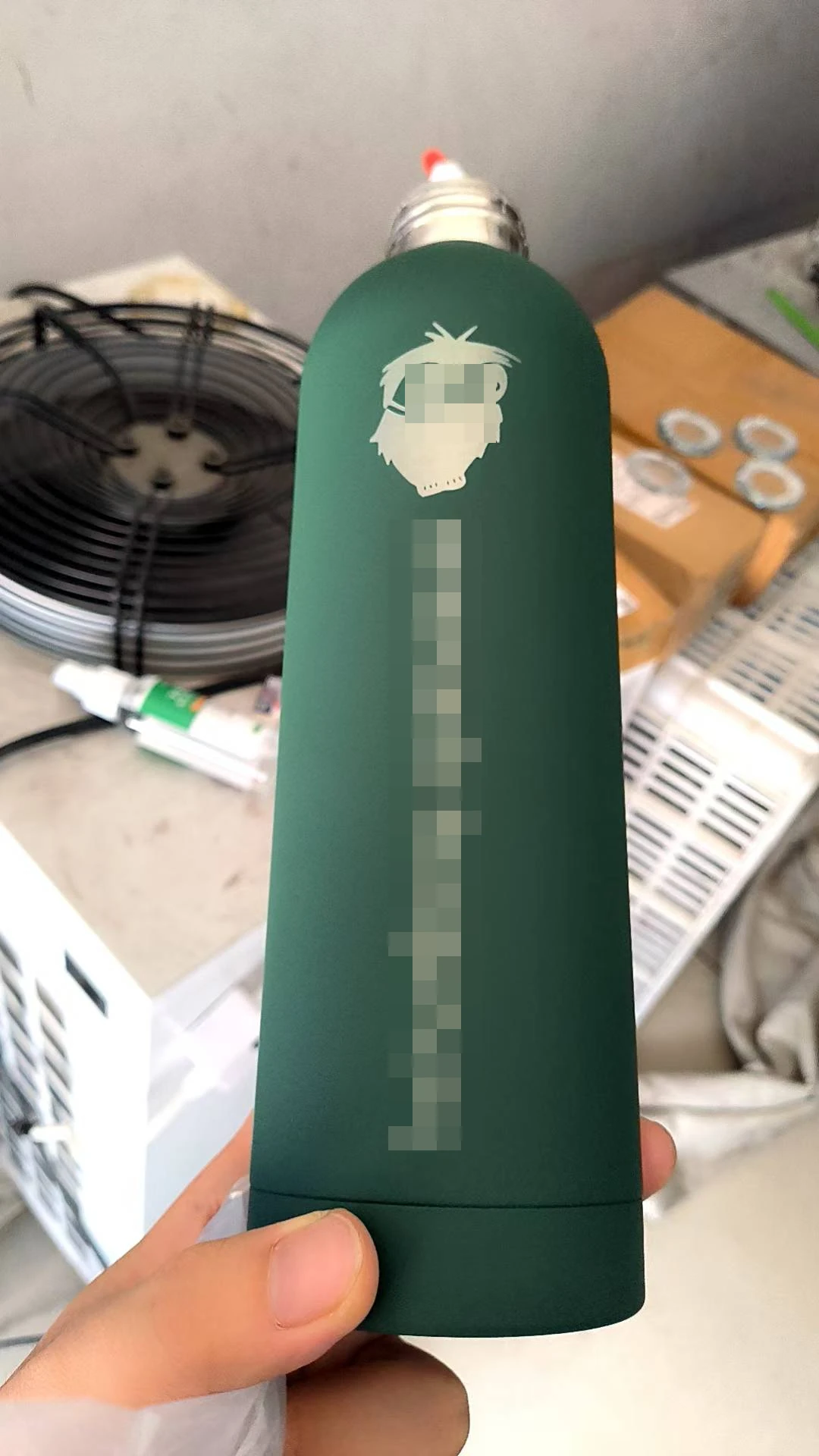 Metallic laser-engraved design on a green bottle, with customer text and part of the motif obscured